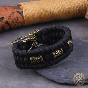 Puede incluir: Pulsera trenzada negra con detalles met&aacute;licos color bronce. La pulsera presenta cuentas decorativas y un cierre detallado con un dise&ntilde;o vikingo. Un accesorio elegante.
