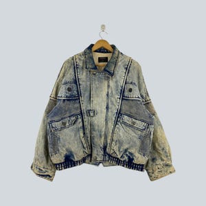Peut inclure: Une veste en jean délavé à l'acide à manches longues avec un col rabattu, une fermeture boutonnée sur le devant et plusieurs poches utilitaires. La veste présente des empiècements en maille bleu foncé sur la poitrine et les manches, avec un ourlet côtelé.