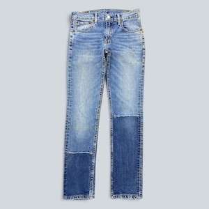 Könnte beinhalten: Eine hellblaue Jeans aus Denim im klassischen Fünf-Taschen-Design mit Knopfverschluss. Der Stoff zeigt eine verwaschene Optik mit aufgesetzten, dunkelblauen Flicken an den unteren Beinpartien, die einen deutlichen Kontrast erzeugen.