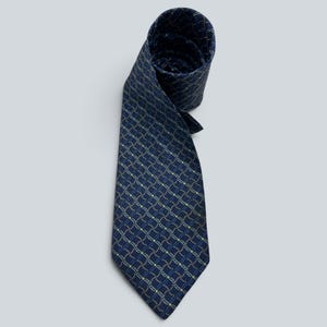 May include: A dark blue necktie featuring a repeating geometric pattern of small, light blue and yellow squares connected by thin, wavy lines. The tie is rolled at the top, showing the fabric texture and the consistent print across the surface.