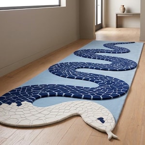 May include: A rectangular area rug featuring a large, winding snake design. The snake has a white head and neck with a mosaic-like pattern, transitioning into a long, dark blue body with a similar white grid pattern that curves across a light blue background.