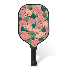 May include: A pickleball paddle with a black handle and a floral design. The paddle face features a pattern of pink and green flowers on a light pink background. The handle is wrapped in black grip tape.