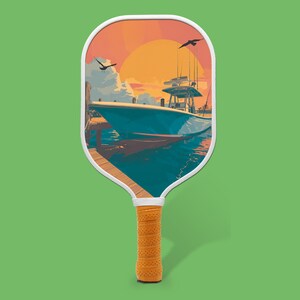 May include: Pickleball paddle featuring a sunset scene with a boat at a pier. The paddle has a white border, a yellow grip, and a green background. The image depicts a boat on the water.