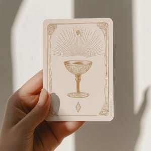 Può includere: Una carta dei tarocchi con un calice dorato con dettagli intricati, su sfondo crema. La carta ha un bordo decorativo e un disegno a raggi di sole sopra il calice. La carta è tenuta in mano.