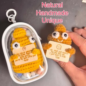 Può includere: Emoji cacca all'uncinetto giallo fatto a mano con occhi mobili, che tiene un cartello di legno. Uno è in una custodia trasparente con perline colorate. Il cartello dice "Sono piccolo e inutile. Nessuno mi ama. Voglio solo nascondermi. TOM."
