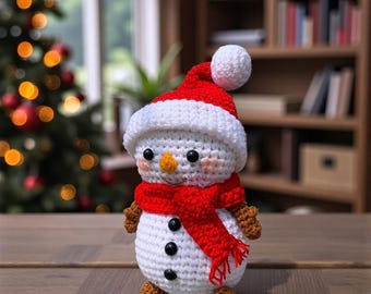 May include: A crocheted snowman figure, wearing a red hat and scarf, with black button eyes and a carrot nose. The snowman is white with brown arms and feet. The background features a Christmas tree and a bookshelf.