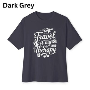 May include: Dark grey t-shirt with the text "Travel is my Therapy" in white. The design includes a plane, globe, camera, and other travel-related icons. The shirt is a crew neck style.