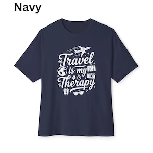 May include: Navy blue t-shirt with the text "Travel is my Therapy" in white. The design includes a plane, globe, camera, and other travel-related icons. The shirt is a short-sleeved crew neck.