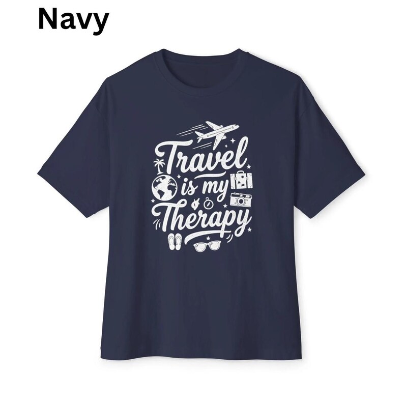 May include: Navy blue t-shirt with the text "Travel is my Therapy" in white. The design includes a plane, globe, camera, and other travel-related icons. The shirt is a short-sleeved crew neck.