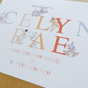 K&ouml;nnte beinhalten: Eine wei&szlig;e Karte mit dem Namen "CELYN RAE" in orangefarbenen und grauen Buchstaben, verziert mit Zeichentrickfiguren wie Dumbo, Bambi und Thumper. Die Karte enth&auml;lt auch den Text "CHRISTENED ON 14/08/22 AT ST TYSUL CHURCH."