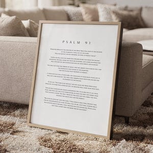 May include: A framed wall art print featuring the full text of Psalm 91 in a clean, black serif font on a white background. The frame is a light-toned wood with a simple, thin profile, displaying the religious scripture clearly in English.