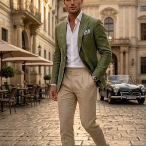 Op de afbeelding: Een olijfgroene blazer gedragen over een wit overhemd met knopen en een beige pantalon met plooien. De outfit bevat een wit pochet, een zilveren polshorloge en lichtbruine loafers, wat zorgt voor een gecoördineerde en verzorgde uitstraling.