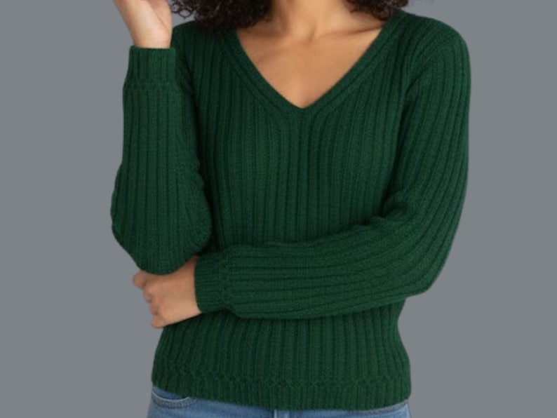 May include: A dark green ribbed knit sweater with a V-neck. The long-sleeved sweater is made of a soft material and is a solid color. The model is wearing blue jeans.