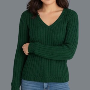 May include: A dark green, ribbed knit sweater with a V-neck. The long-sleeved top is made of a soft material and is paired with blue jeans. The sweater's texture and color create a classic, comfortable look.