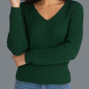 May include: A dark green, ribbed knit sweater with a V-neck. The long sleeves are cuffed at the wrists. The sweater is made of a soft, comfortable material. The model is wearing blue jeans.