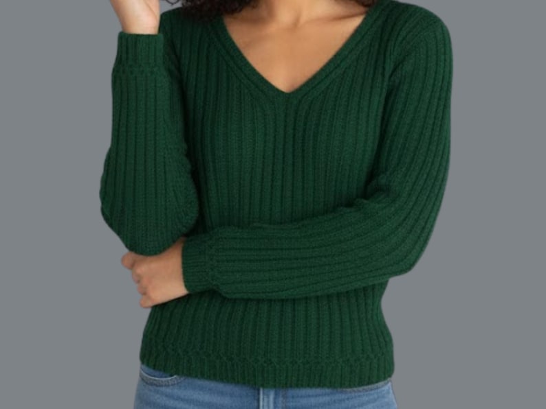 May include: A dark green, ribbed knit sweater with a V-neck. The long sleeves are cuffed at the wrists. The sweater is made of a soft, comfortable material. The model is wearing blue jeans.