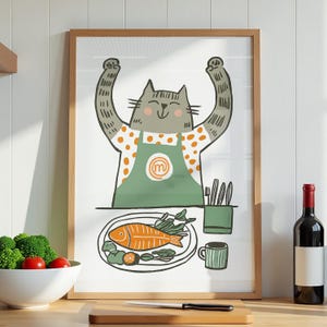 May include: A framed print featuring a cartoon cat chef with its arms raised. The cat wears a green apron and is standing in front of a plate with a fish. A wine bottle and vegetables are also visible.