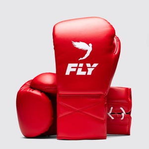 Può includere: Un paio di guantoni da boxe rossi con la scritta "FLY" in lettere bianche e una grafica alata bianca. I guantoni sono realizzati in un materiale liscio e sono mostrati su sfondo bianco.