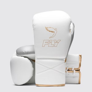 Può includere: Guantoni da boxe bianchi con finiture dorate e la scritta "FLY" in oro. I guantoni presentano una figura alata dorata sopra la scritta "FLY". I guantoni sono in pelle e hanno un accento argentato sul retro.
