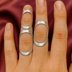May include: Silver-toned finger rings with an oval design. The rings are worn on the fingers, with one ring on the tip of the finger and another ring on the middle of the finger. The rings are made of a shiny metal.