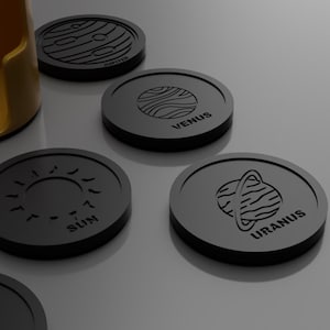 May include: Black coasters with planet designs, including Jupiter, Venus, Uranus, and the Sun. Each coaster features a unique planet illustration and name in a simple, modern font. A yellow holder is visible in the background.