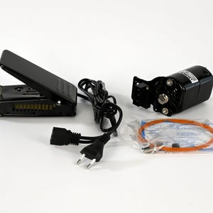 May include: A black sewing machine motor kit with a foot pedal, power cord, and an orange belt. The motor is mounted on a bracket. The foot pedal is rectangular and has a hinged top.