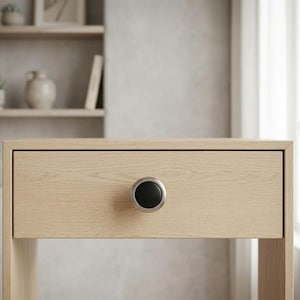 May include: Close-up of a light-colored wooden drawer with a black and silver knob. The drawer is part of a larger piece of furniture, possibly a nightstand or desk. The wood grain is visible.