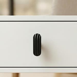 May include: A close-up of a white drawer with a black, vertically-oriented, ribbed handle. The handle is oval-shaped and has a series of curved grooves. The drawer is part of a larger piece of furniture.