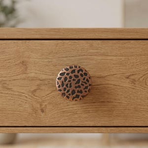 May include: Close-up of a wooden drawer with a round, copper-colored knob. The knob has a textured, spotted pattern. The drawer is made of light-colored wood with visible grain.