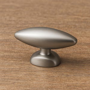 May include: A brushed nickel cabinet knob with a rounded base and an oval top. The hardware is designed for furniture and has a modern, minimalist aesthetic. The knob is shown against a wood grain background.