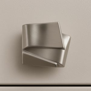 May include: A modern, brushed nickel cabinet knob with a geometric, angular design. The knob has a square base and a faceted, three-dimensional shape, offering a contemporary aesthetic. The hardware is shown against a neutral background.