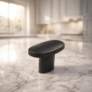May include: A black cabinet knob with an oval top and a cylindrical base. The hardware is made of a dark, possibly metal material, and is set against a blurred kitchen background. The knob is designed for easy grip and adds a modern touch.