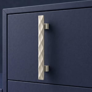 May include: A close-up of a navy blue cabinet with a cream-colored, geometric-patterned handle. The handle is a vertical bar with a series of diamond shapes carved into it. The cabinet has a simple, modern design.