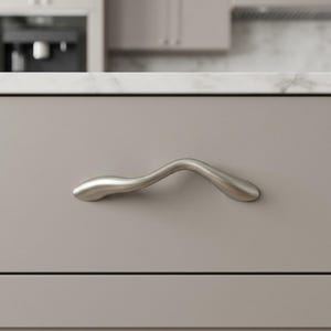 May include: A brushed nickel cabinet pull with a curved, organic design. The handle is mounted on a light gray cabinet door, offering a modern aesthetic. The pull is a single piece, with a smooth, matte finish, and is designed for easy gripping.