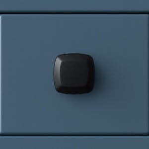 May include: Close-up of a dark blue drawer front with a square, black cabinet knob. The knob is centered on the drawer and has rounded edges. The drawer front is a solid, matte blue color.