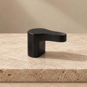 May include: A matte black faucet handle with a smooth, curved, and elongated L-shaped design. The handle features a solid, minimalist construction with a rounded top surface and a vertical base, providing a clean and functional aesthetic.