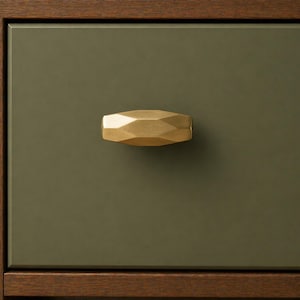 May include: Close-up of a gold-colored, geometric drawer pull on an olive green drawer. The drawer is framed by a dark brown wooden border. The pull has a faceted design, reflecting light. This hardware is suitable for furniture.