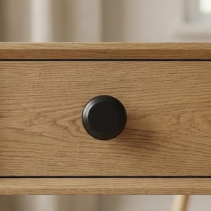 May include: Close-up of a wooden drawer with a black, round knob. The drawer is made of light-colored wood with visible grain. The knob is centered on the drawer front, providing a simple, modern aesthetic. The image highlights the texture of the wood and the knob's design.