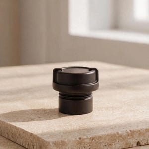 May include: A matte dark brown cylindrical bottle stopper featuring a flat top surface with two small protruding side tabs and a threaded base section designed for insertion into a bottle opening, showcasing a solid and uniform color.