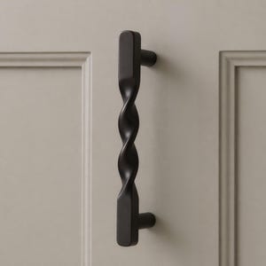 May include: A black, twisted cabinet pull with a rectangular base and a cylindrical knob. The handle is mounted on a light gray cabinet door. The design features a spiral pattern, adding a decorative element to the hardware.