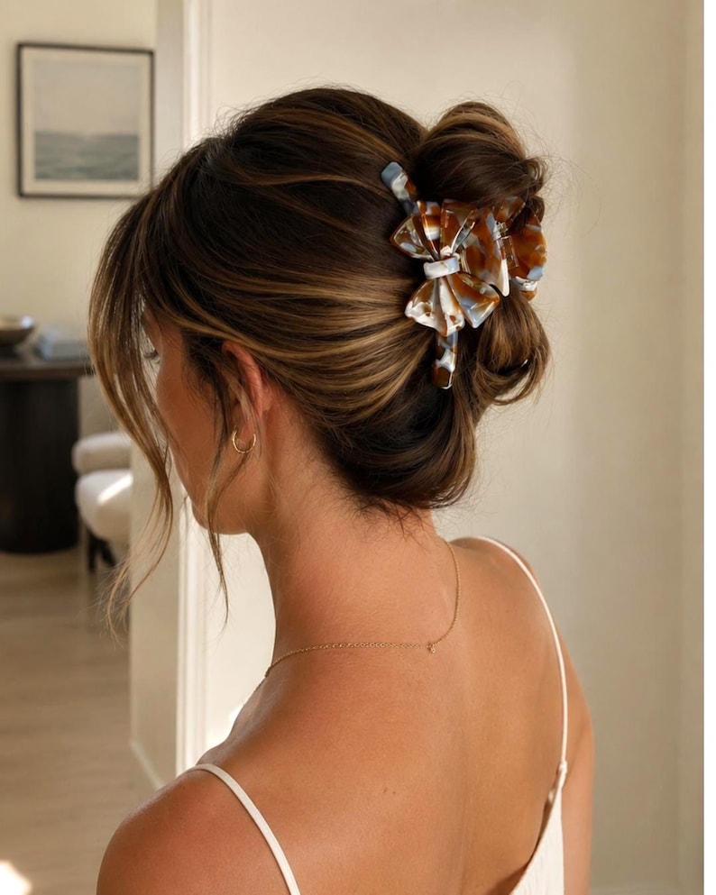 Pu&ograve; includere: Un fermaglio per capelli con motivo tartarugato multicolore nei toni del marrone, bianco e blu. Il fermaglio ha un design a forma di fiocco con finitura lucida ed &egrave; fissato nei capelli castano scuro, raccolti in uno chignon morbido.