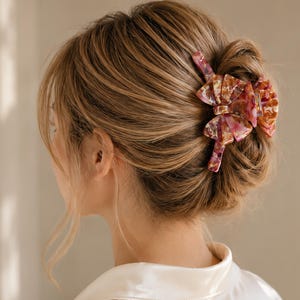 Pu&ograve; includere: Un fermaglio per capelli con un design a fiocco a pi&ugrave; strati e un motivo marmorizzato nei toni del rosa, dell'arancione e del bianco. L'accessorio &egrave; realizzato in un materiale lucido e traslucido, fissato in uno chignon per tenere i capelli.