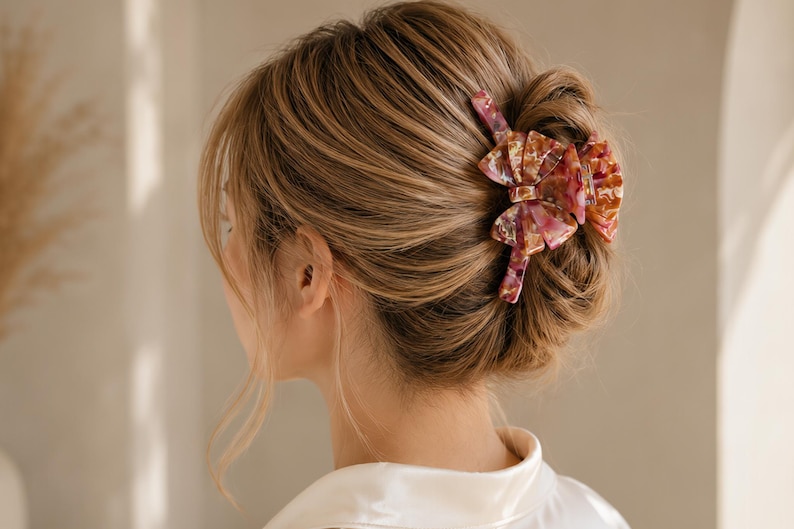 Pu&ograve; includere: Un fermaglio per capelli con un design a fiocco a pi&ugrave; strati e un motivo marmorizzato nei toni del rosa, dell'arancione e del bianco. L'accessorio &egrave; realizzato in un materiale lucido e traslucido, fissato in uno chignon per tenere i capelli.