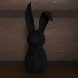 May include: A black decorative rabbit figurine with long ears and a textured, ribbed surface. The bunny is made of a solid material and stands upright. The background is a wooden surface.