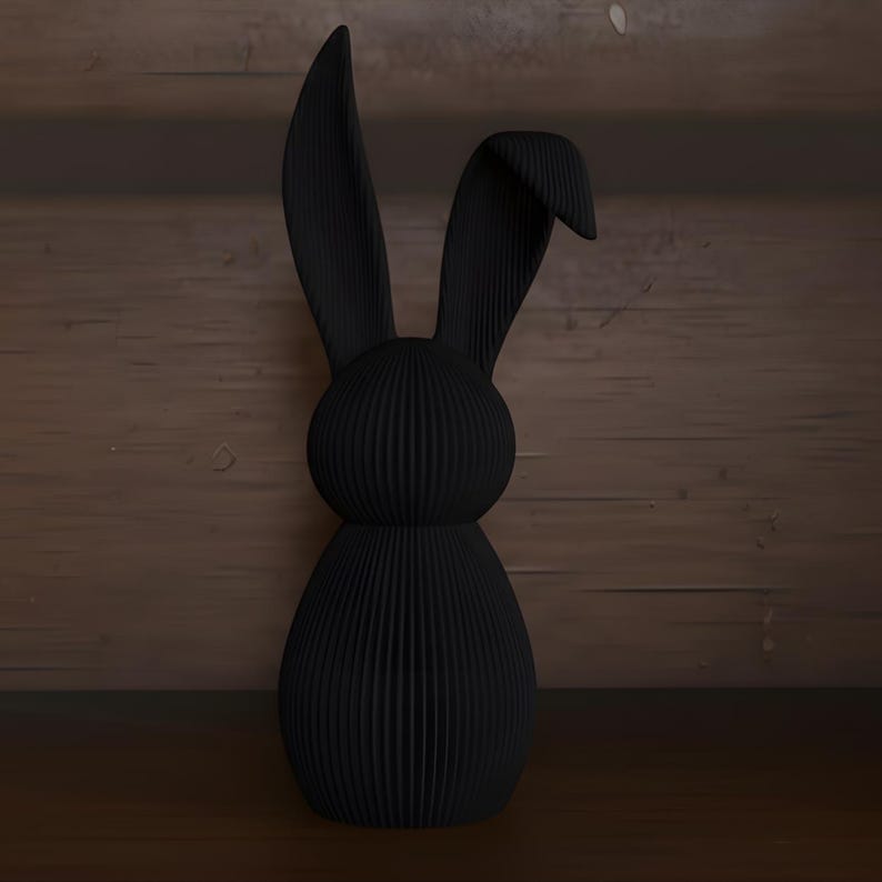 May include: A black decorative rabbit figurine with long ears and a textured, ribbed surface. The bunny is made of a solid material and stands upright. The background is a wooden surface.