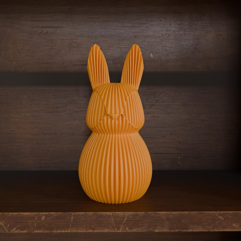 May include: An orange, textured rabbit figurine with vertical lines, standing on a wooden shelf. The bunny has long ears and a rounded body, and is set against a dark wood background.