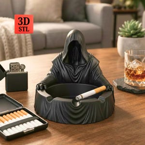 Op de afbeelding: Zwarte asbak in de vorm van een figuur met capuchon, met een sigaret. Een zwarte aansteker en een sigarettenkoker liggen op tafel. De afbeelding heeft een 3D STL-logo.