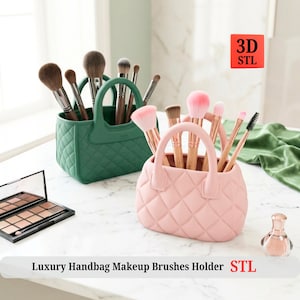 Op de afbeelding: Twee handtasvormige make-up kwasten houders, één groen en één roze, gevuld met kwasten. De houders hebben een gewatteerd patroon en handvatten. De tekst "Luxury Handbag Makeup Brushes Holder STL" staat onderaan.