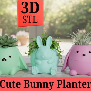 May include: Three pastel-colored bunny planters. The planters are mint green, light blue, and pink. Each planter has a different plant inside. The text "3D STL" and "Cute Bunny Planter" are displayed in the image.