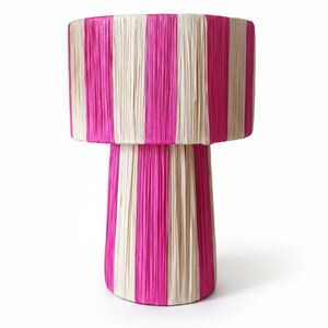 Peut inclure: Une lampe décorative avec un abat-jour et une base cylindriques. La lampe présente des rayures verticales de rose vif et de matériau crème. La lampe a un design superposé, l'abat-jour étant plus large que la base.